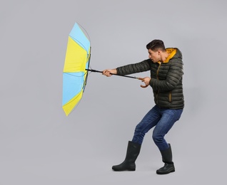 Photo of Emotional man with umbrella caught in gust of wind on grey background
