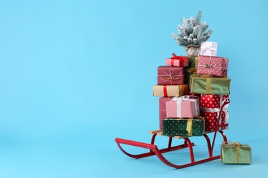 Photo of Sleigh with gift boxes and small fir on light blue background. Space for text