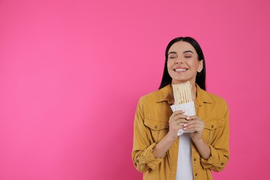Photo of Happy young woman with delicious shawarma on pink background. Space for text