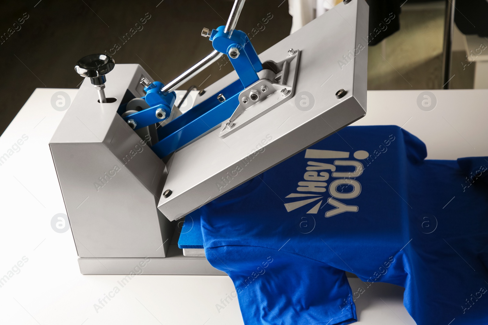 Photo of Printing logo. Heat press with blue t-shirt on white table