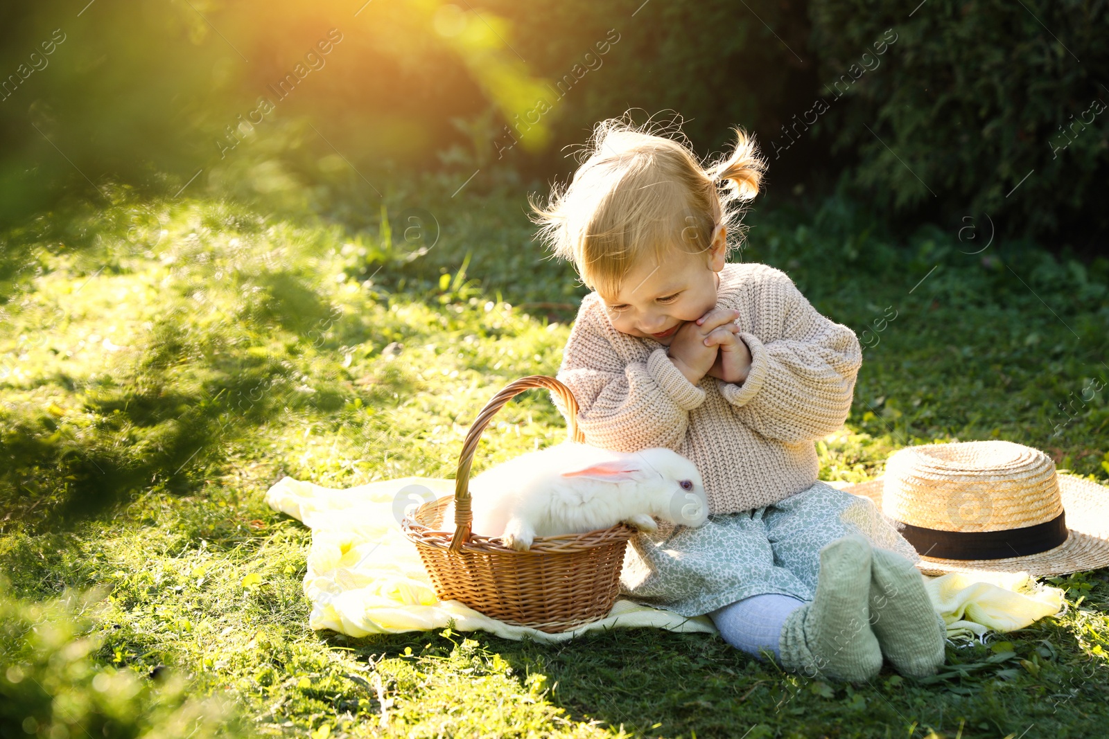 Photo of Happy little girl with cute rabbit on green grass outdoors