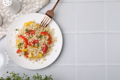 Plate of cooked bulgur with vegetables on white tiled table, top view. Space for text