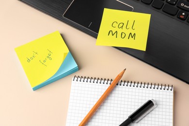 Paper notes with reminders, notebook and laptop on beige table, above view