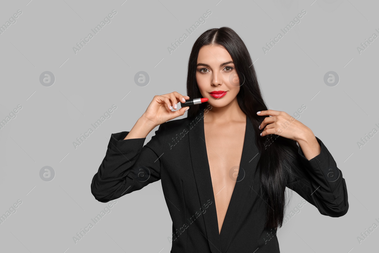 Photo of Young woman with beautiful makeup holding red lipstick on light gray background