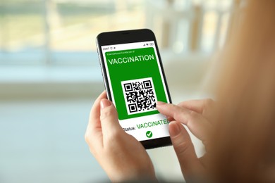 Image of Woman holding smartphone with international certificate of vaccination indoors, closeup