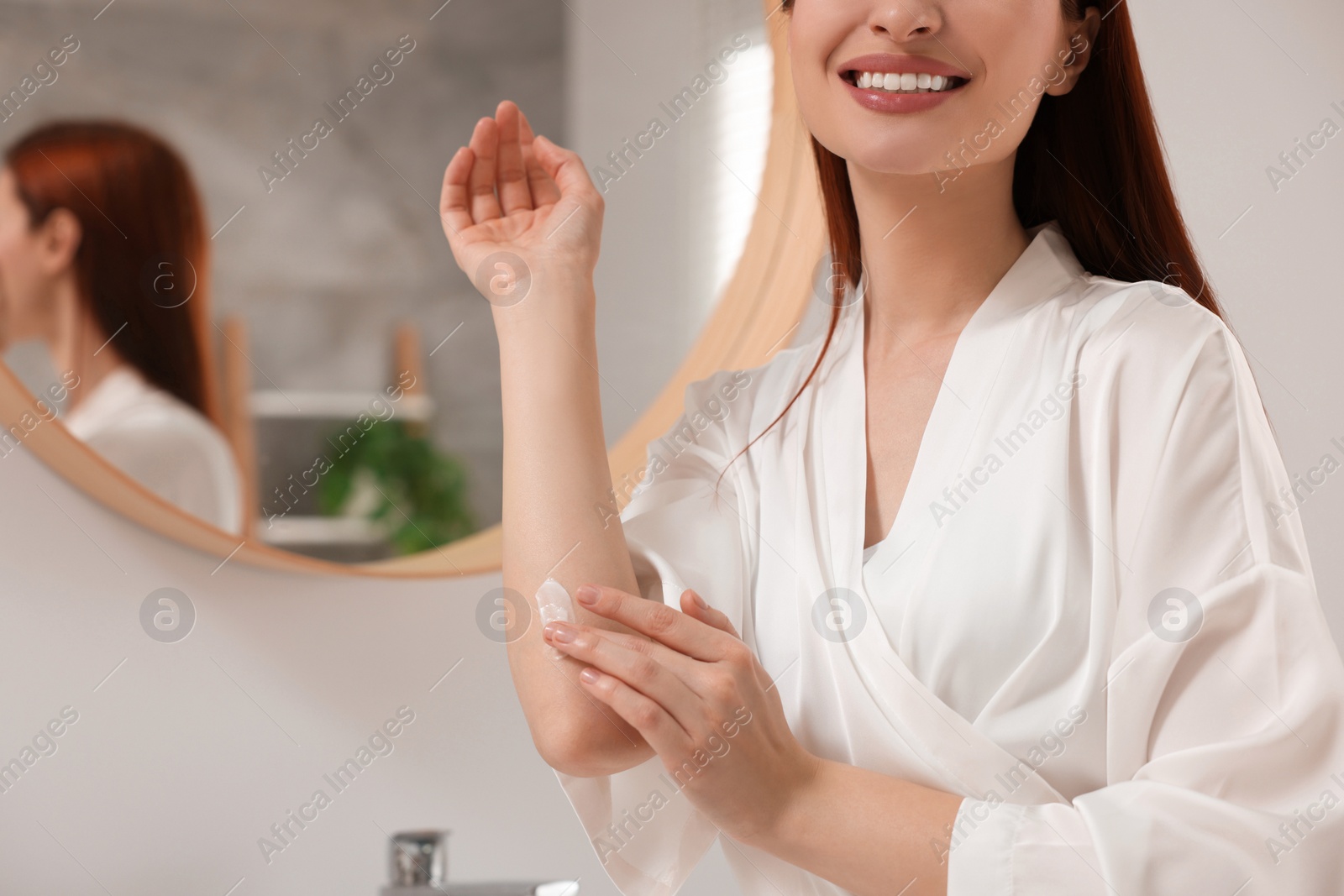 Photo of Young woman applying body cream onto elbow in bathroom, closeup. Space for text