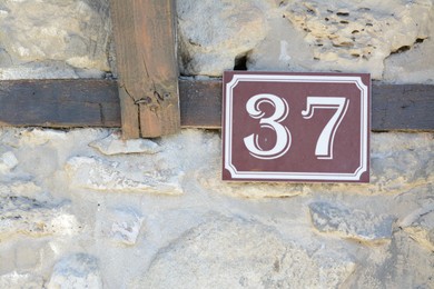 Plate with house number thirty seven on stone wall outdoors, closeup