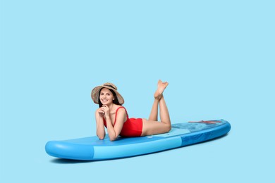 Happy woman resting on SUP board against light blue background