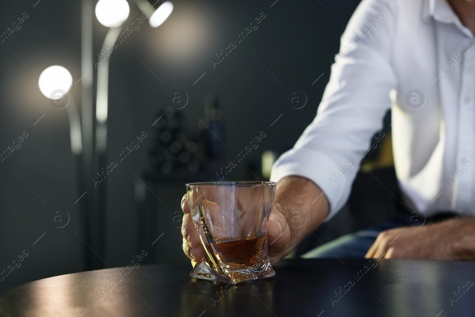 Photo of Man holding glass with whiskey at table, closeup. Space for text