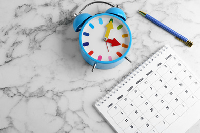 Calendar, pen and alarm clock on white marble background,