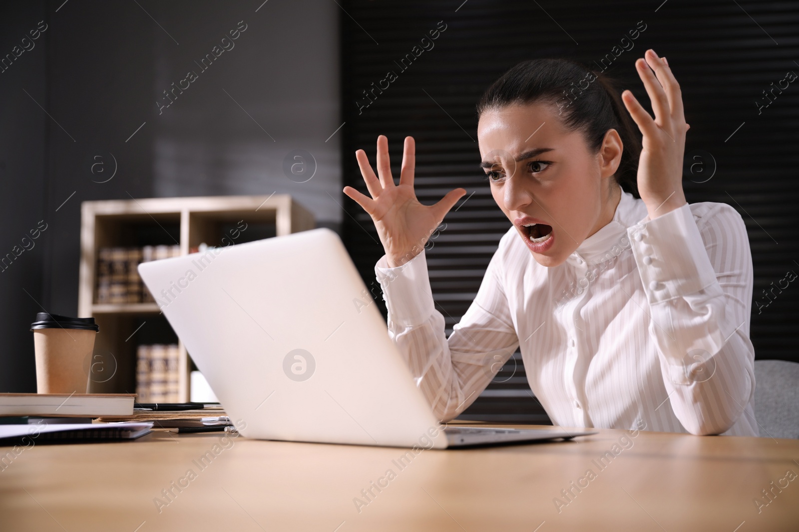 Photo of Emotional young businesswoman working on laptop in office. Online hate concept