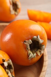 Photo of Delicious ripe persimmons in bowl on table, closeup