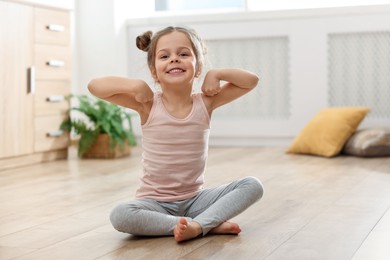 Photo of Little cute girl practicing yoga on floor at home