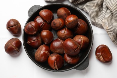 Photo of Fresh edible sweet chestnuts in frying pan on white tiled table, flat lay