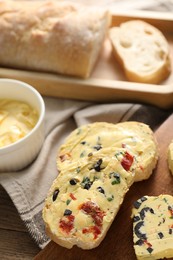 Photo of Tasty butter with olives, chili pepper, parsley and bread on wooden table