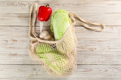 Photo of Fresh Chinese cabbage, bell pepper and garlic in net bag on wooden table, top view