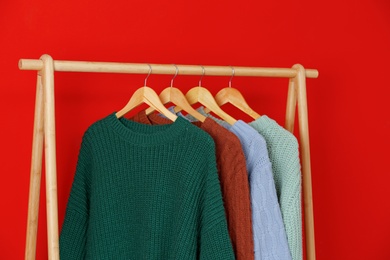 Collection of warm sweaters hanging on rack near red wall