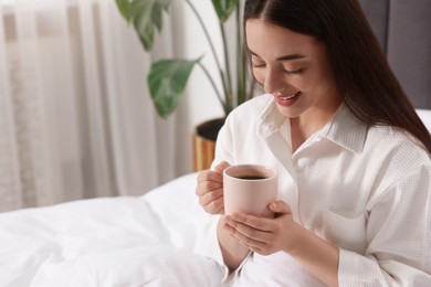 Photo of Happy woman with cup of drink in bed at home, space for text. Lazy morning