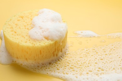 Photo of Sponge with foam on yellow background, closeup
