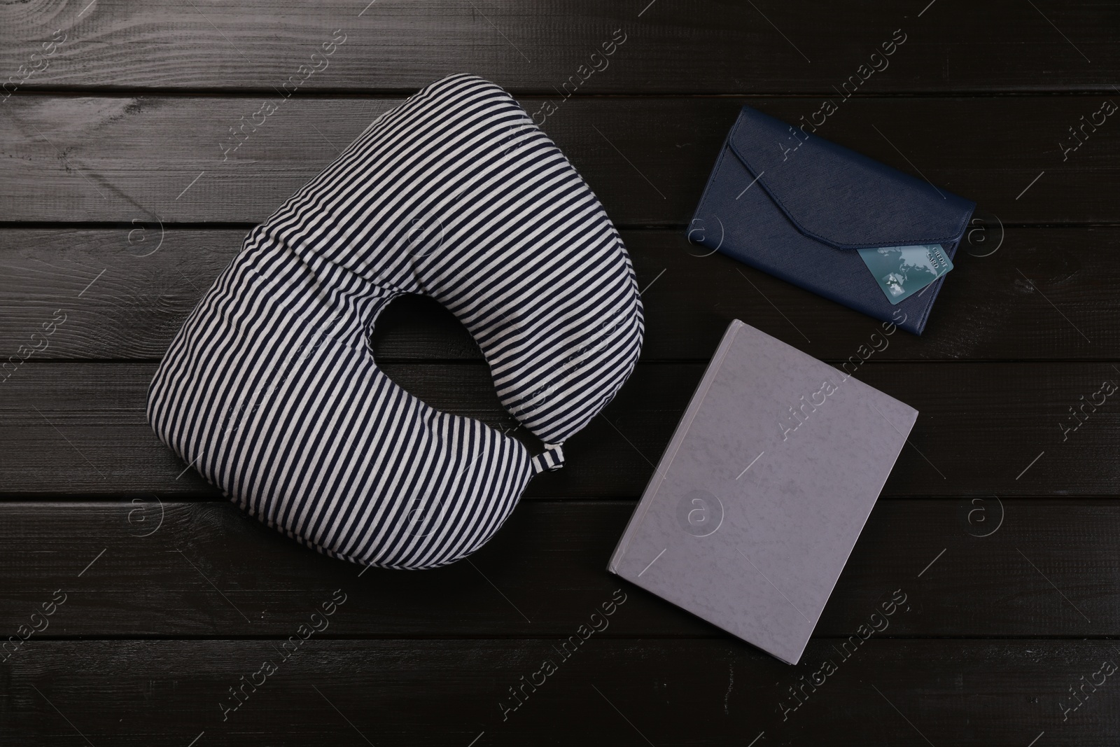 Photo of Striped travel pillow, notebook and wallet with credit card on dark wooden background, flat lay