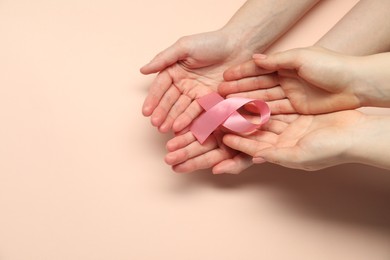 Photo of Breast cancer awareness. Women holding pink ribbon on beige background, top view. Space for text