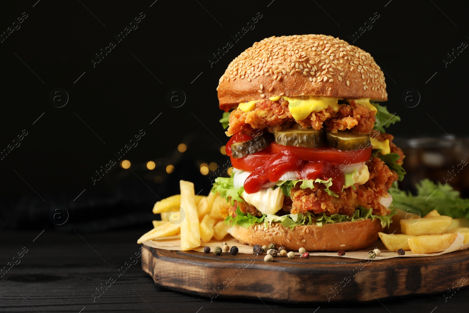 Photo of Delicious burger with crispy chicken patty and french fries on black wooden table. Space for text