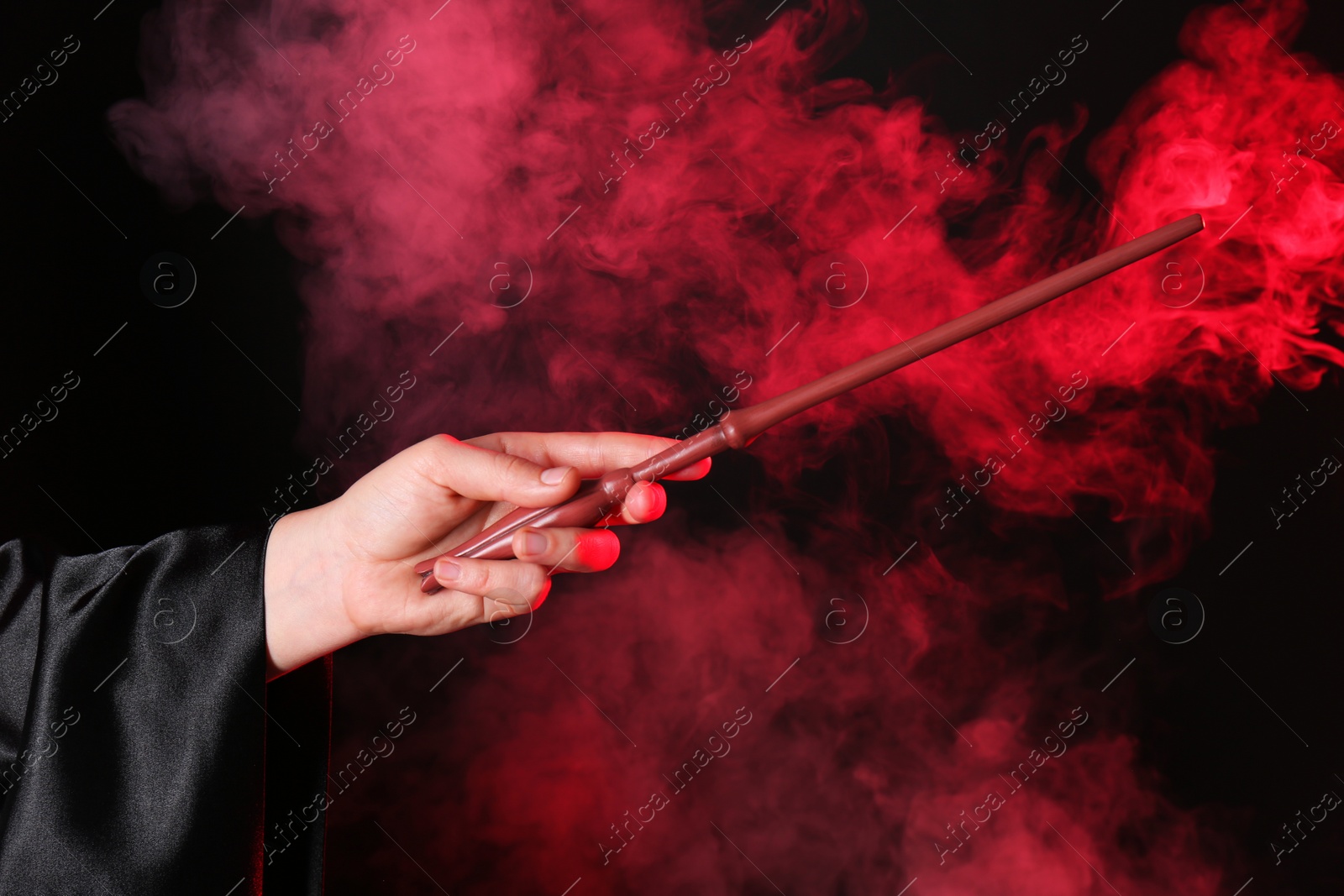 Photo of Magician holding wand in smoke on dark background, closeup