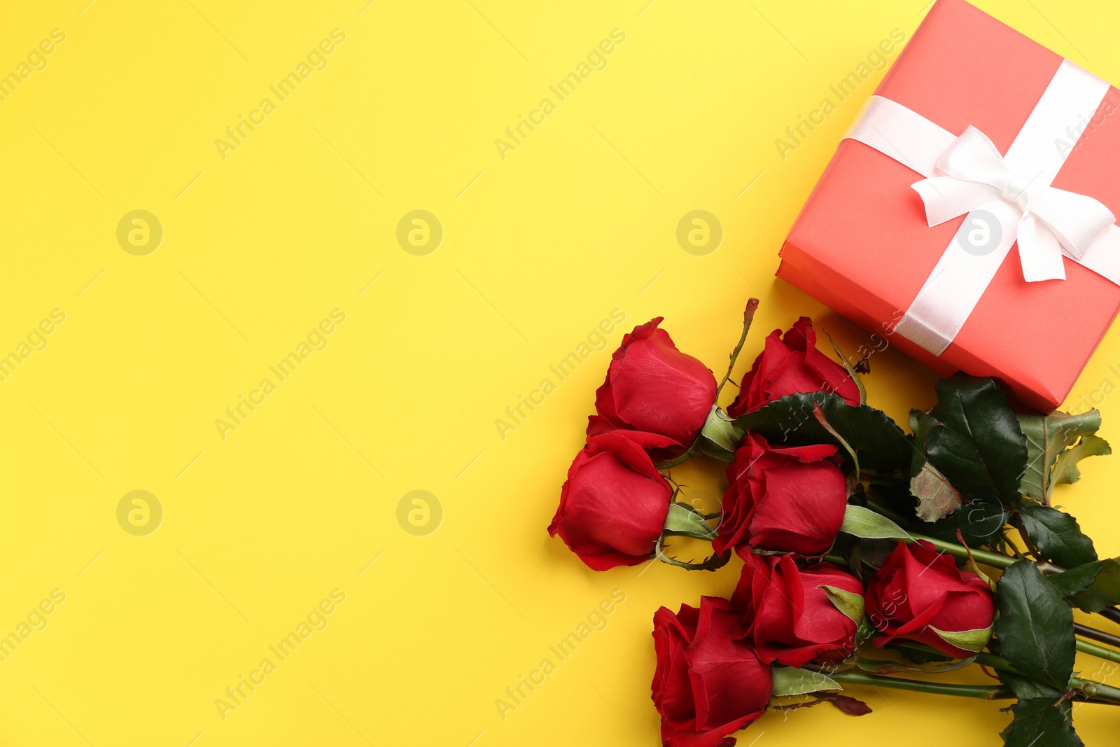 Photo of Beautiful red roses and gift box on yellow background, flat lay with space for text. Valentine's Day celebration