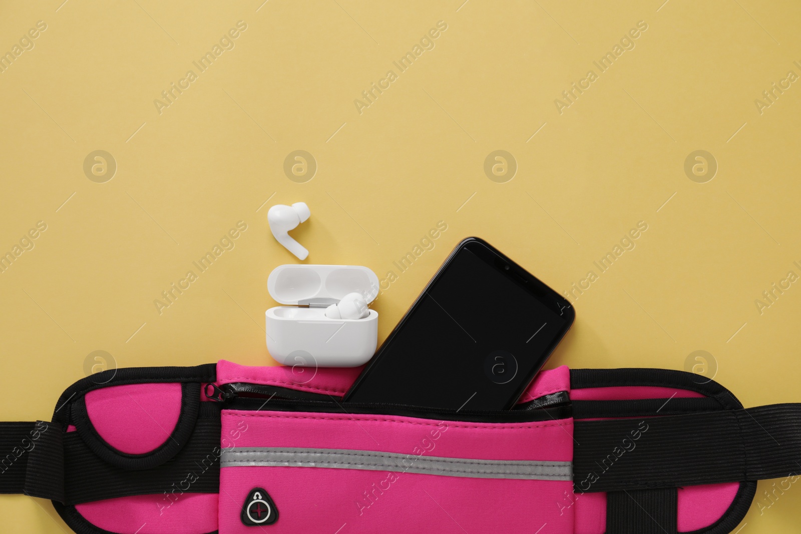 Photo of Stylish pink waist bag with smartphone and earphones on yellow background, flat lay. Space for text