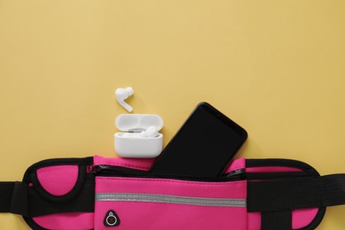 Photo of Stylish pink waist bag with smartphone and earphones on yellow background, flat lay. Space for text
