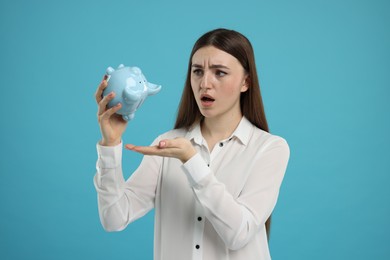 Sad woman with piggy bank on light blue background