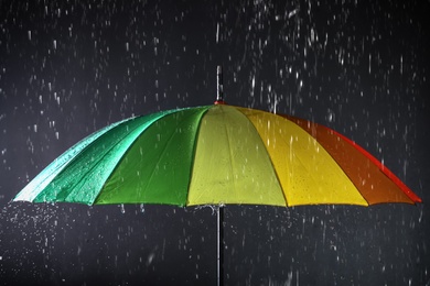 Photo of Bright umbrella under rain on dark background