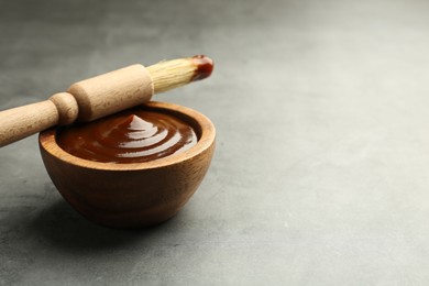 Photo of Tasty barbeque sauce in bowl and brush on grey textured table, closeup. Space for text
