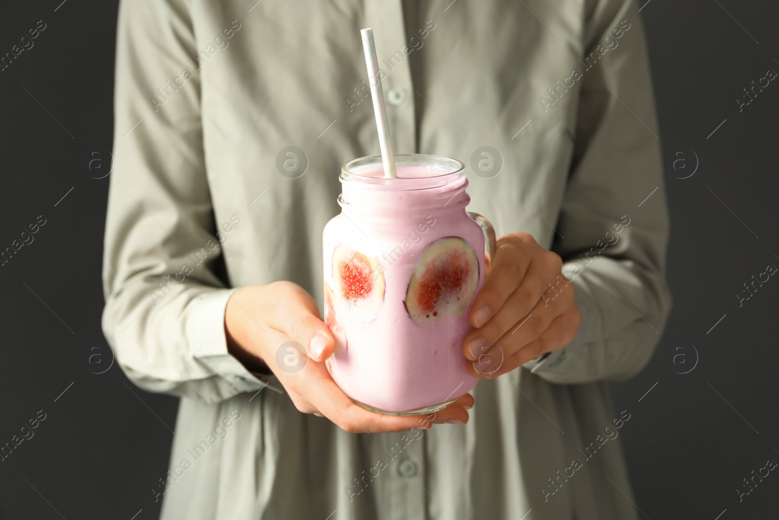Photo of Woman holding mason jar with fig smoothie on grey background, closeup