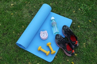 Photo of Alarm clock and morning exercise set on green grass, flat lay