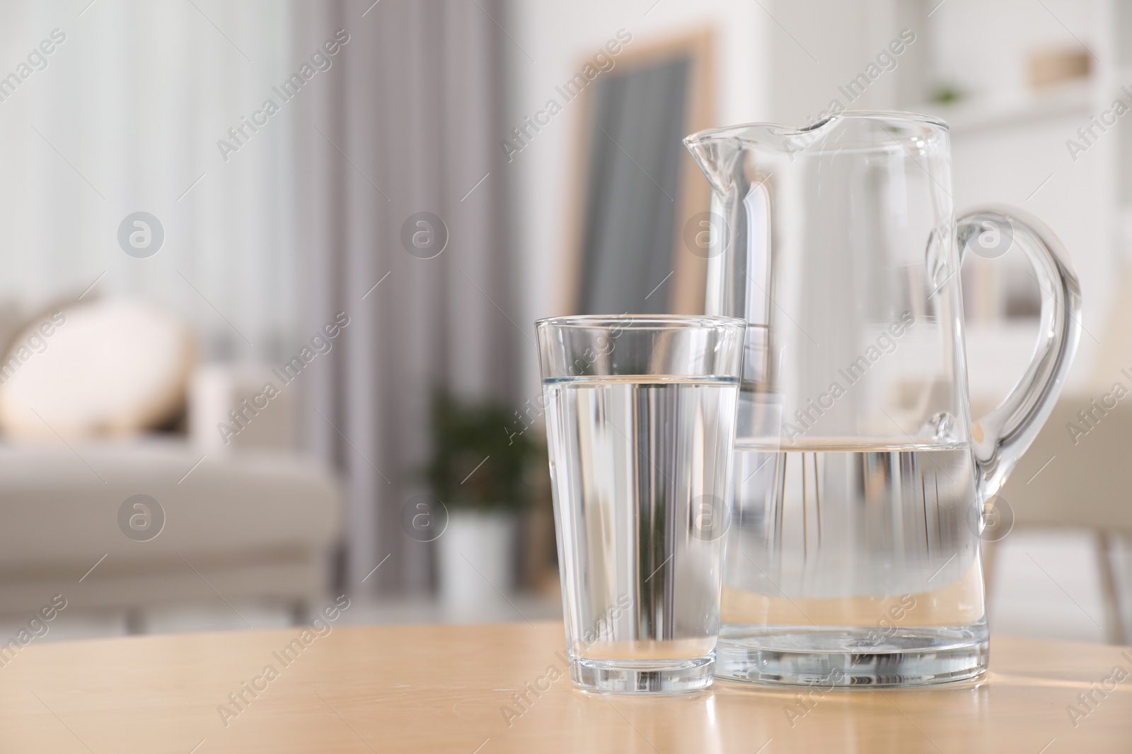 Photo of Jug and glass with clear water on table indoors, closeup. Space for text