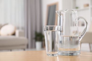 Jug and glass with clear water on table indoors, closeup. Space for text