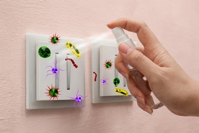 Image of Woman spraying antiseptic onto light switch full of microbes, closeup