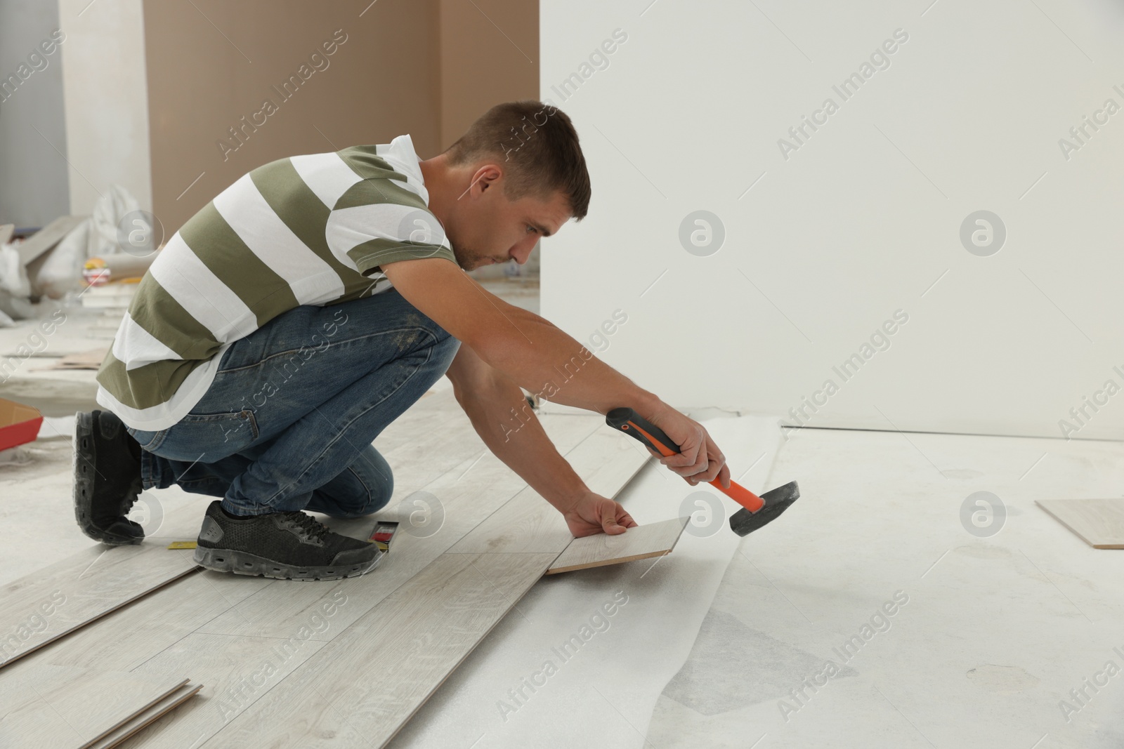 Photo of Professional worker using hammer during installation of new laminate flooring indoors