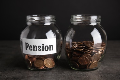 Photo of Glass jars with coins and label PENSION on dark table