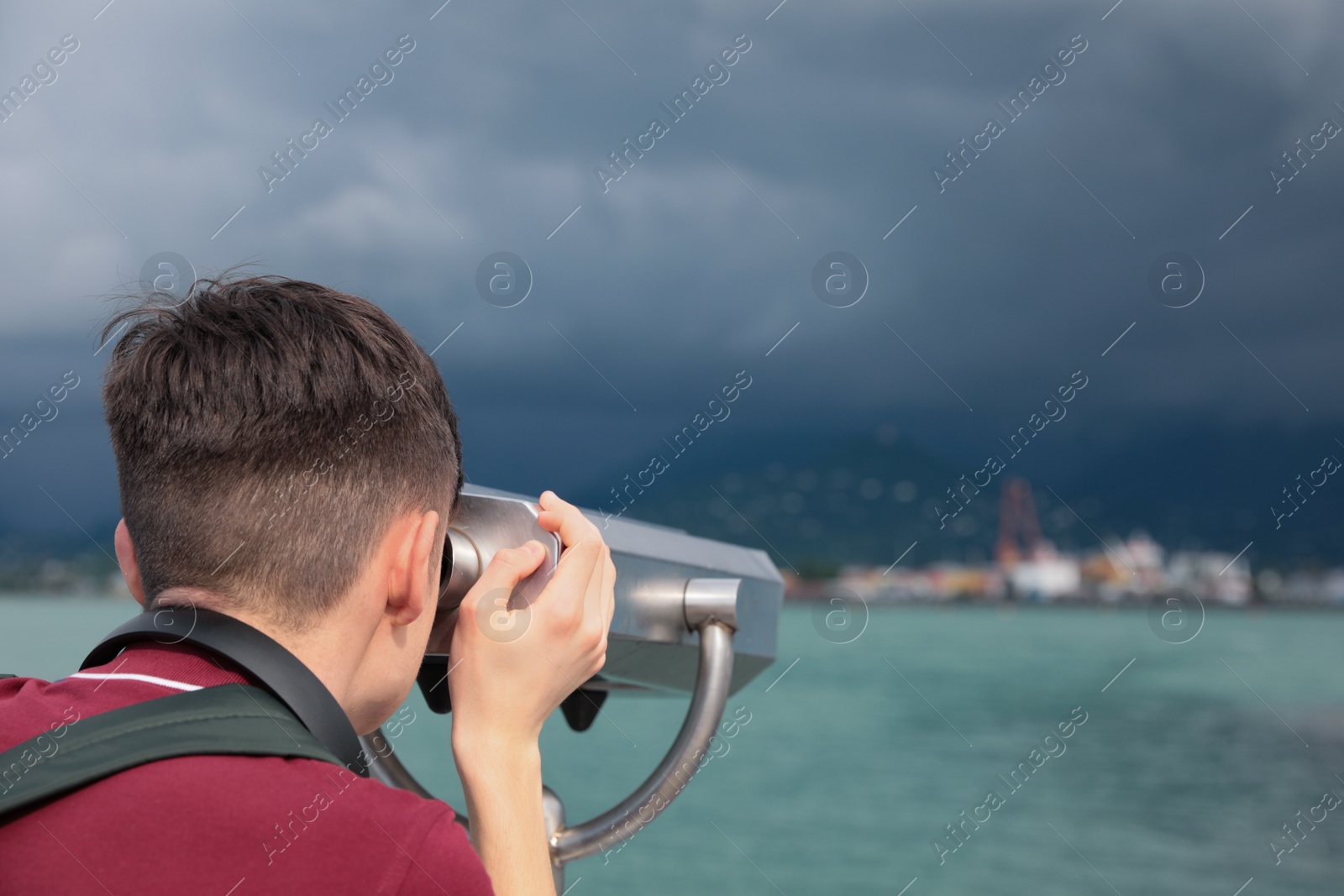 Photo of Teenage boy looking through mounted binoculars at mountains. Space for text