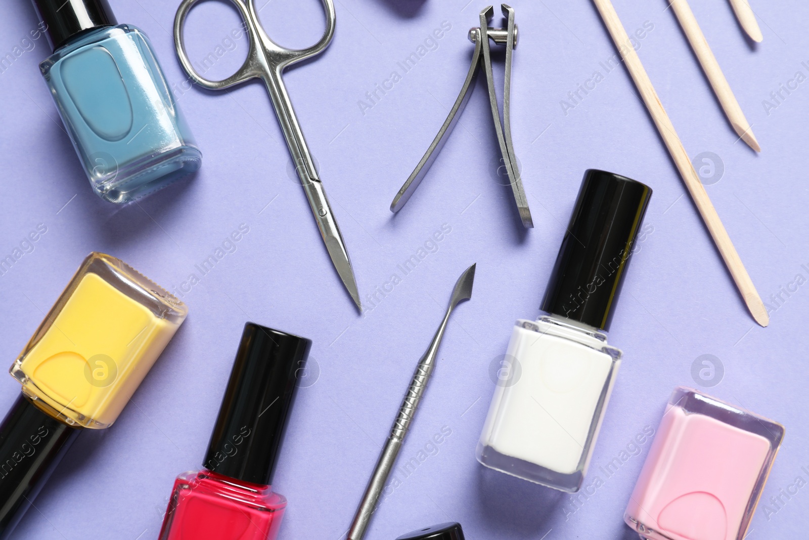 Photo of Nail polishes and set of pedicure tools on lilac background, flat lay
