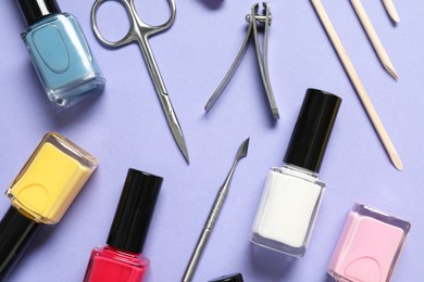 Photo of Nail polishes and set of pedicure tools on lilac background, flat lay