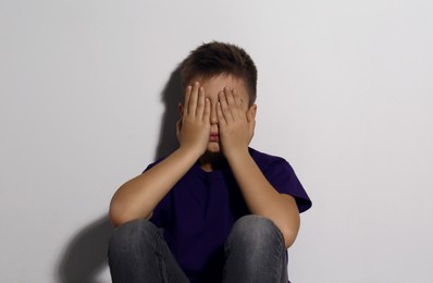 Photo of Abused little boy closing eyes near white wall. Domestic violence concept