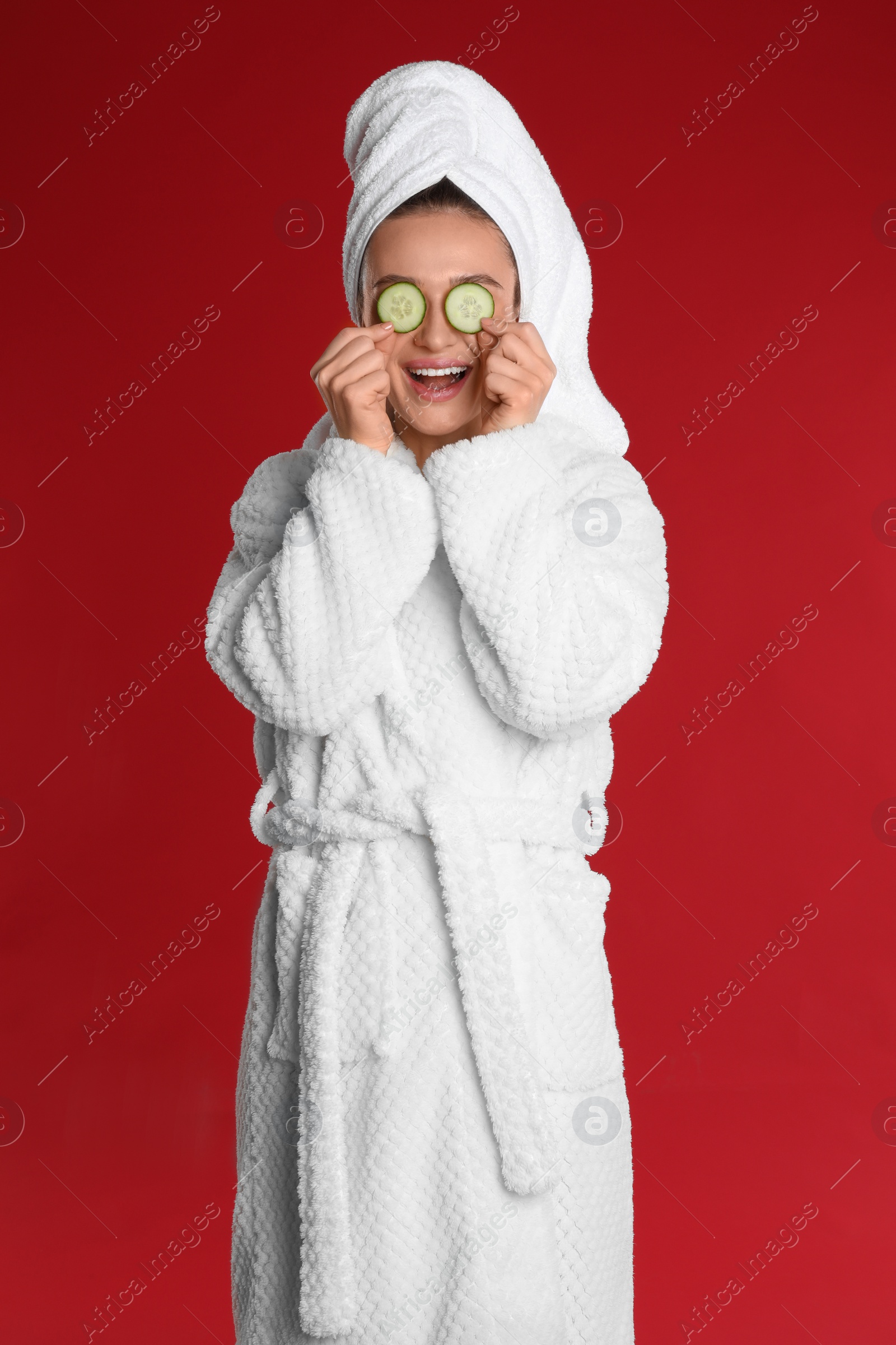 Photo of Young woman in bathrobe with cucumber slices on red background