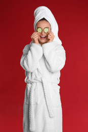 Photo of Young woman in bathrobe with cucumber slices on red background