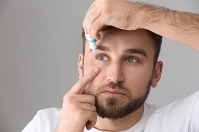 Young man using eye drops on light grey background