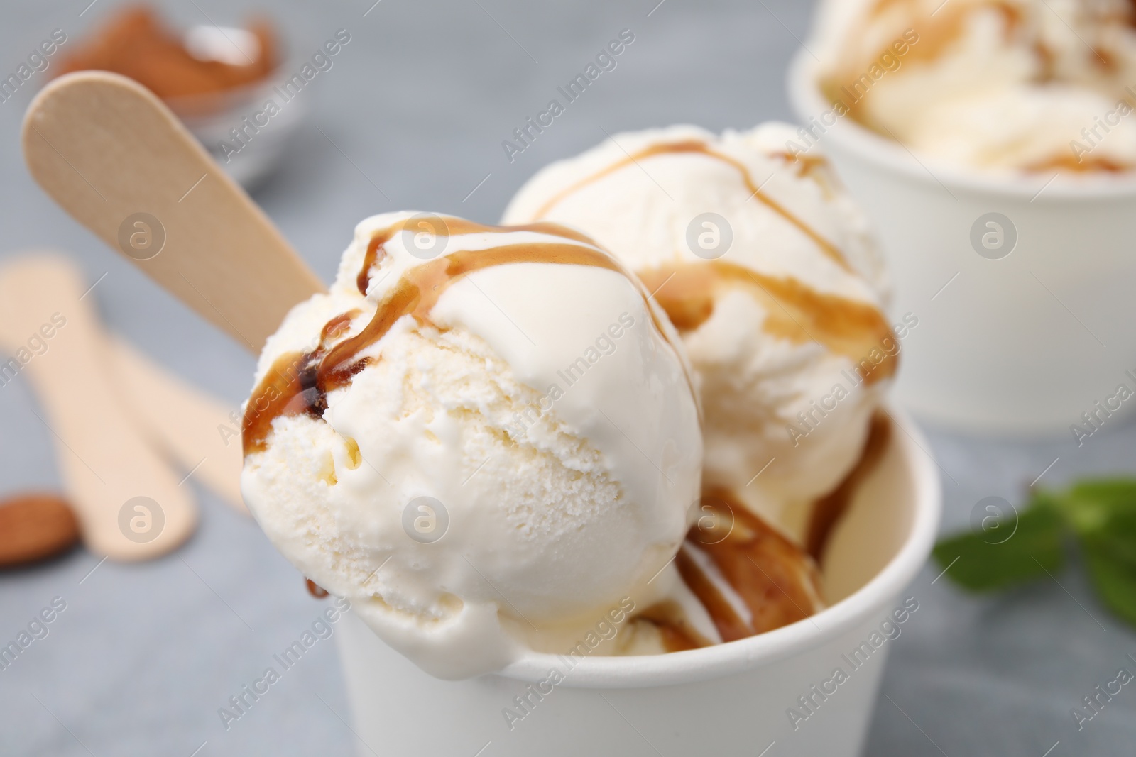 Photo of Scoops of ice cream with caramel sauce in paper cup, closeup