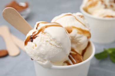 Scoops of ice cream with caramel sauce in paper cup, closeup