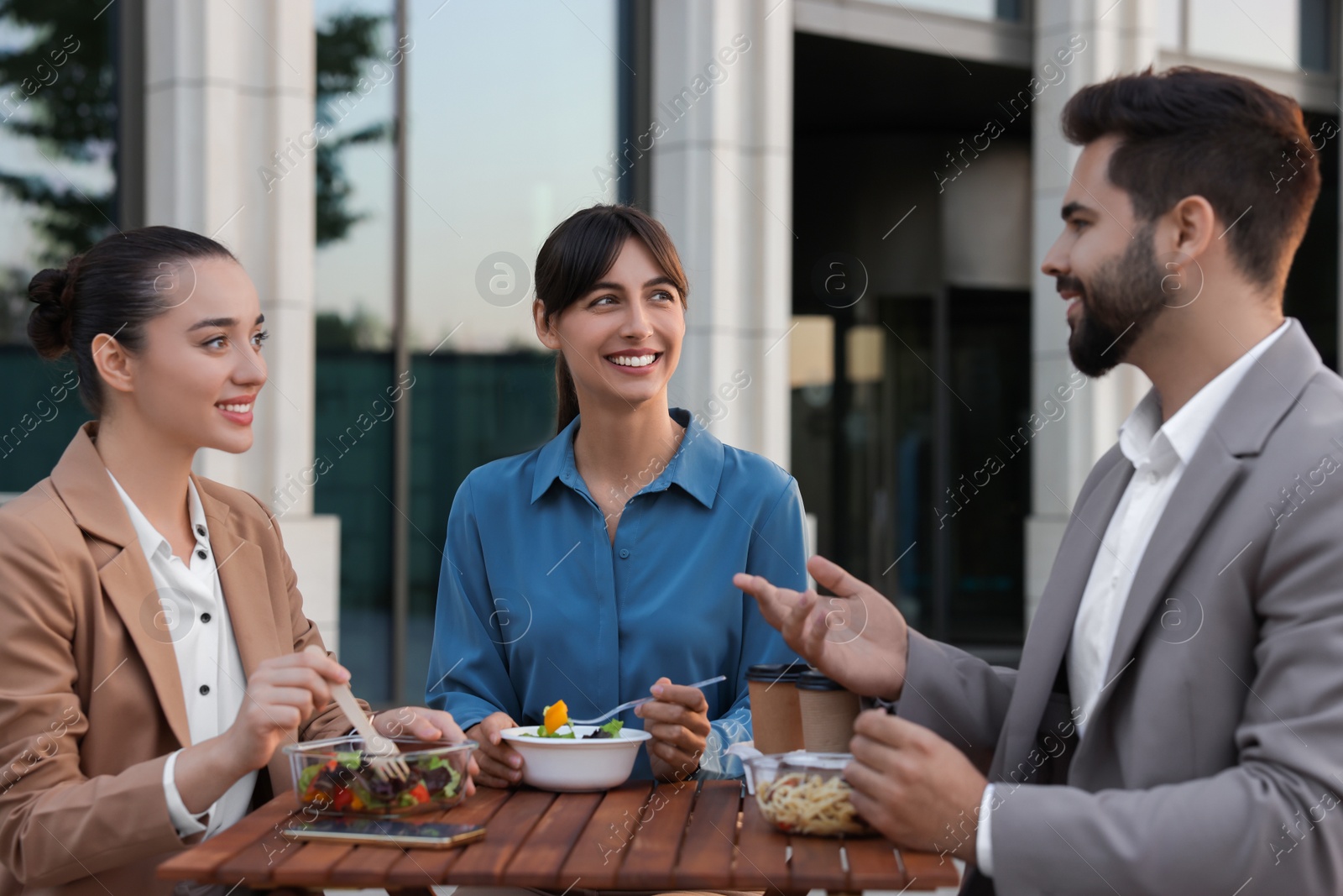 Photo of Business lunch. Happy colleagues spending time together at wooden table during break outdoors